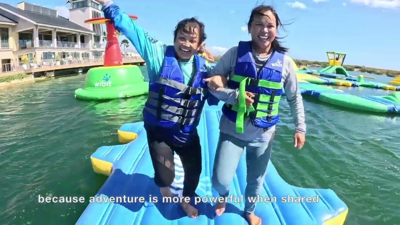 Two Adaptive Adventures participants in life jackets, laughing as they cross a floating water course