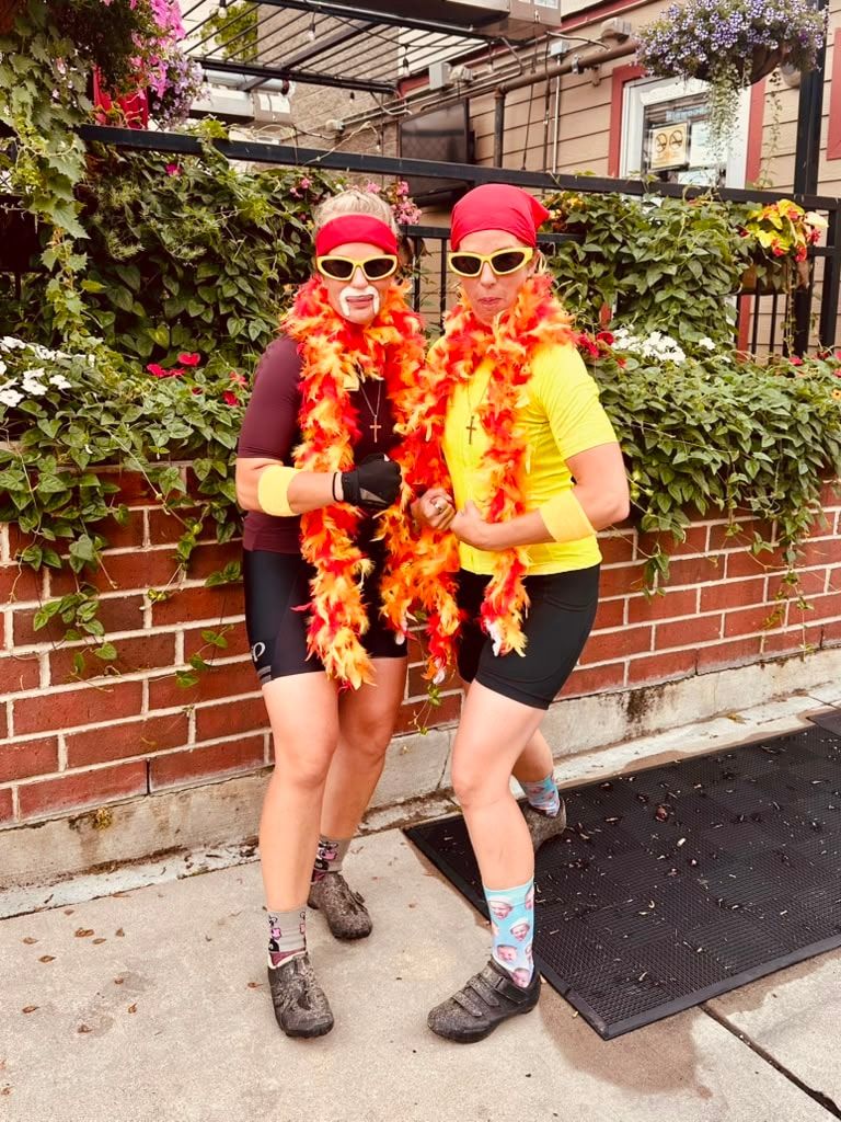 Two riders in matching feather boas and bandanas posing against a brick wall
