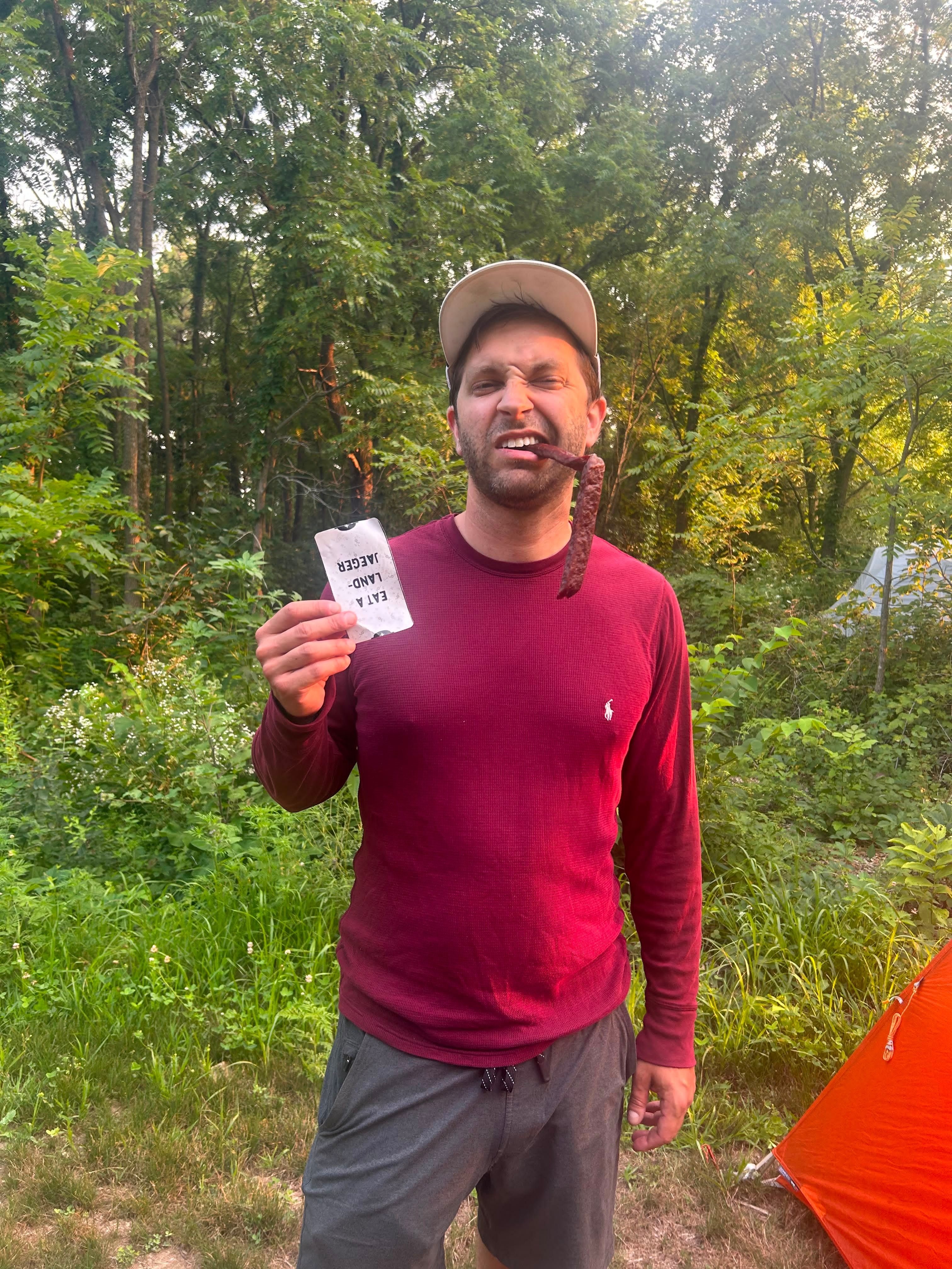 A rider standing beside a tent in the woods holding a tarot card