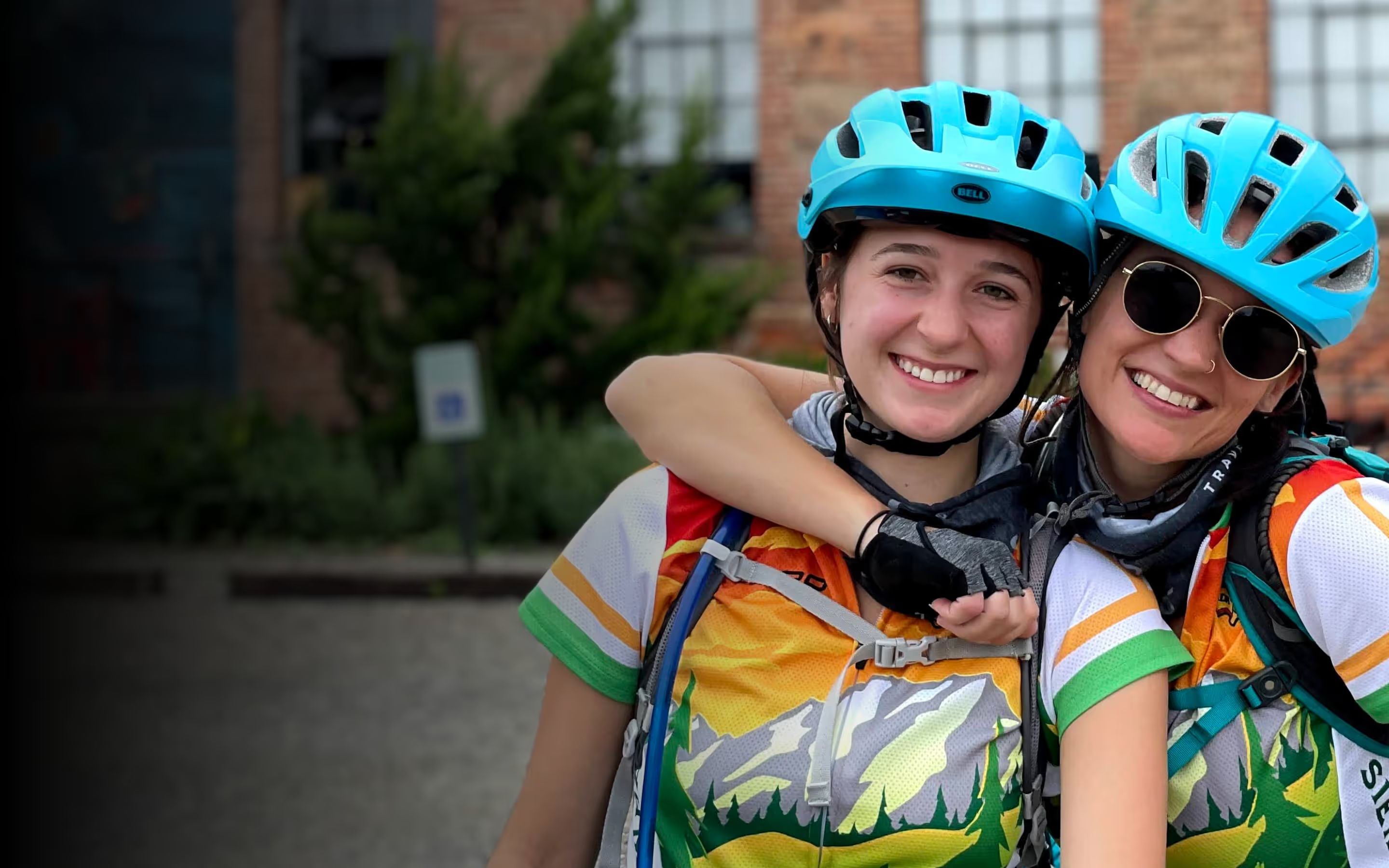 Two riders in cyan helmets laughing with their arms around each other at the start line