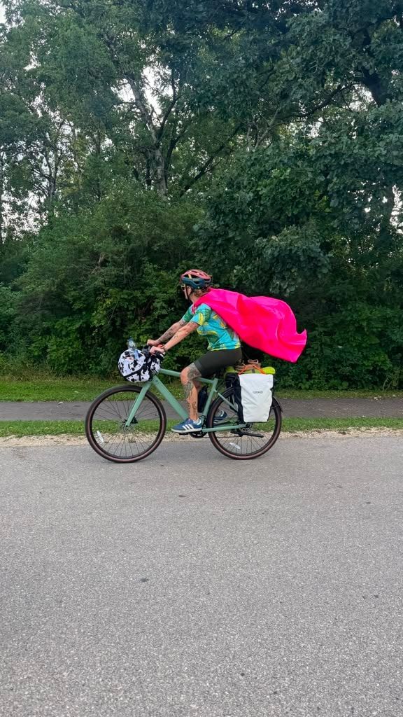 A rider on a paved trail with a bright pink cape flying out behind them
