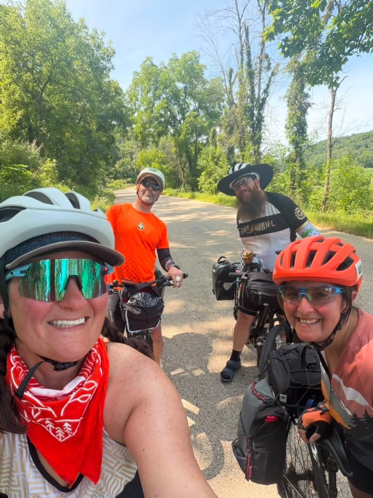 A rider taking a selfie with two others on loaded bikes behind her on a country road