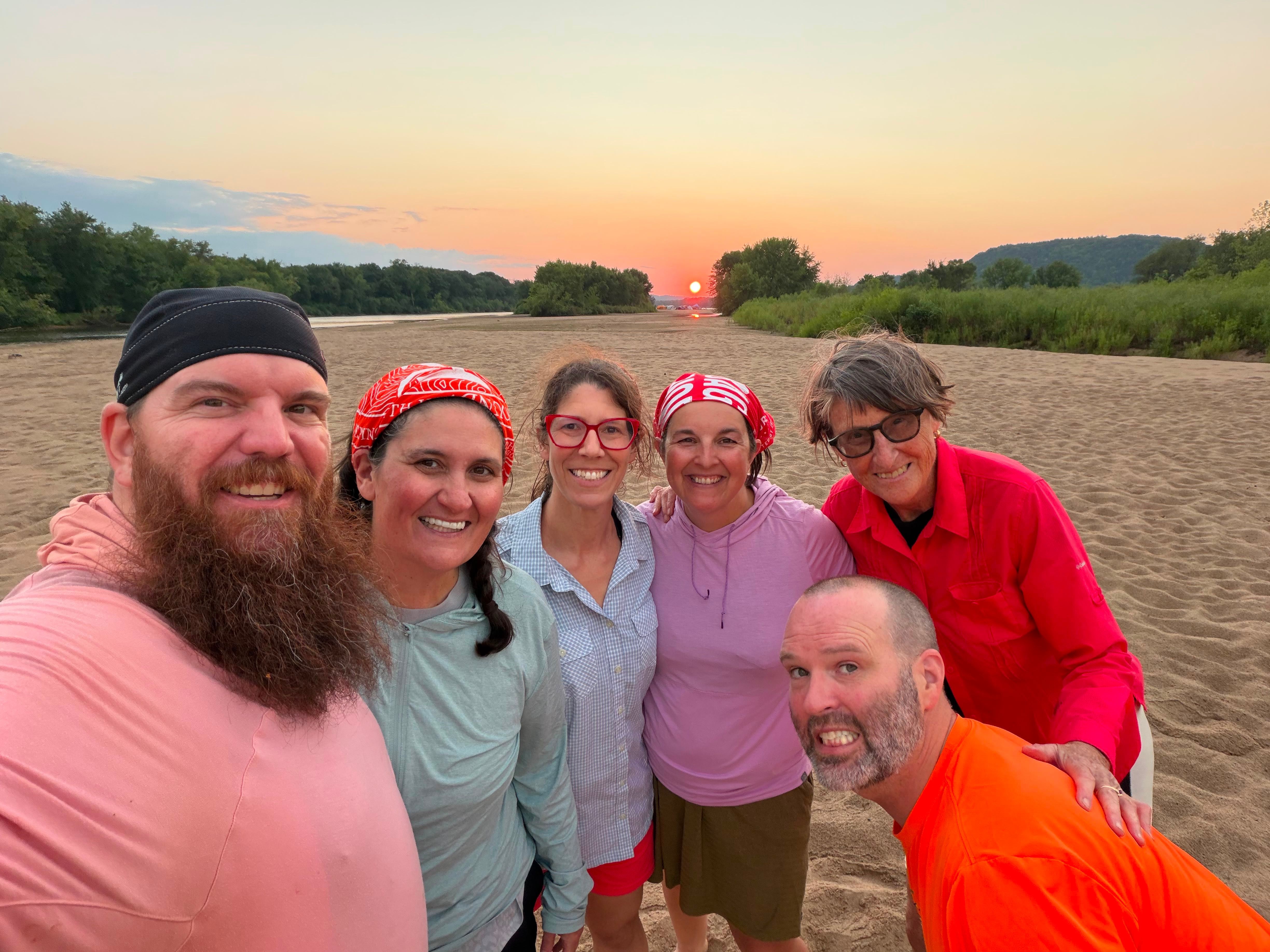 Six riders posing on a river sandbar at sunset