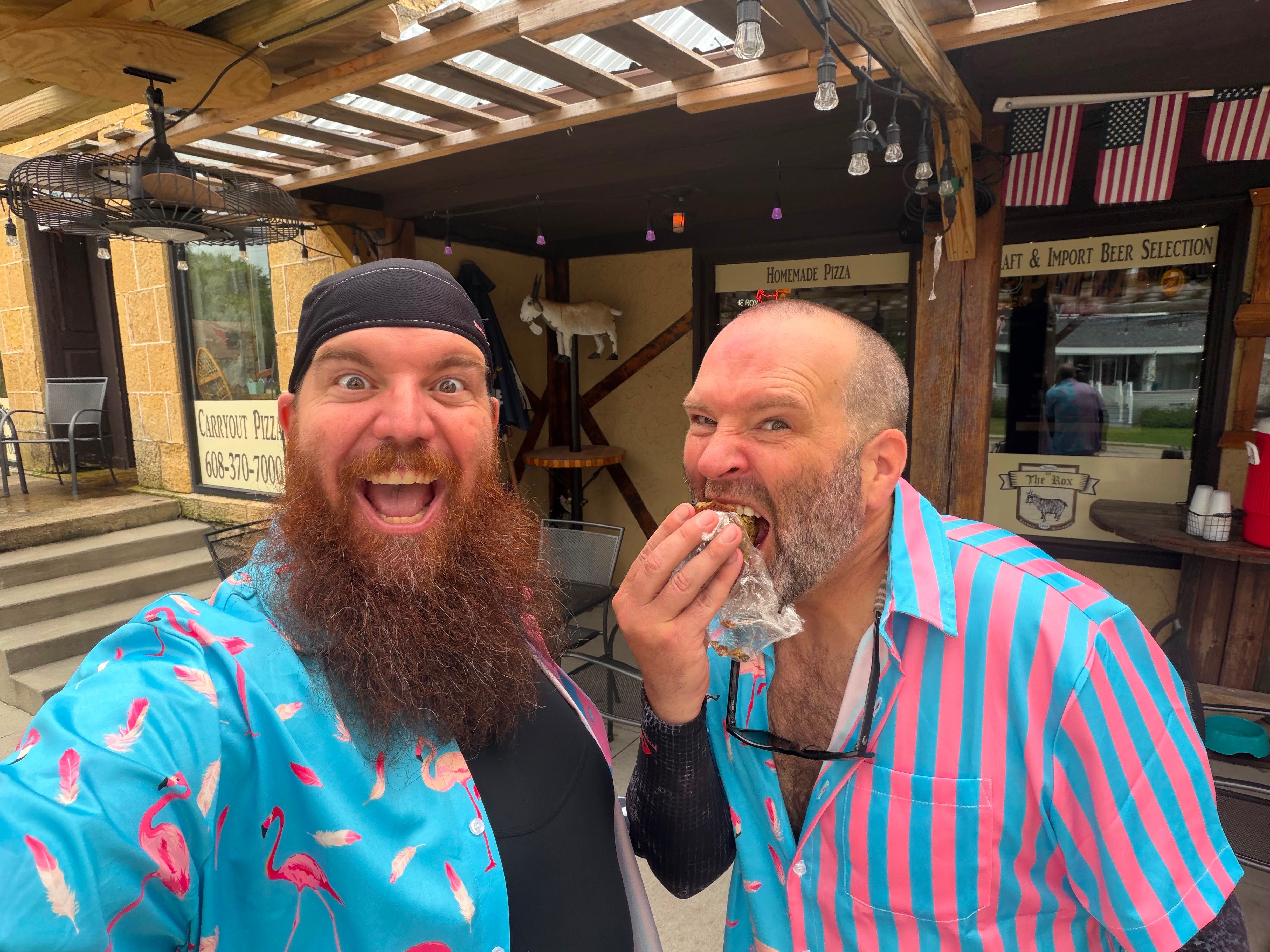 Two riders in loud tropical shirts messing about outside a bar